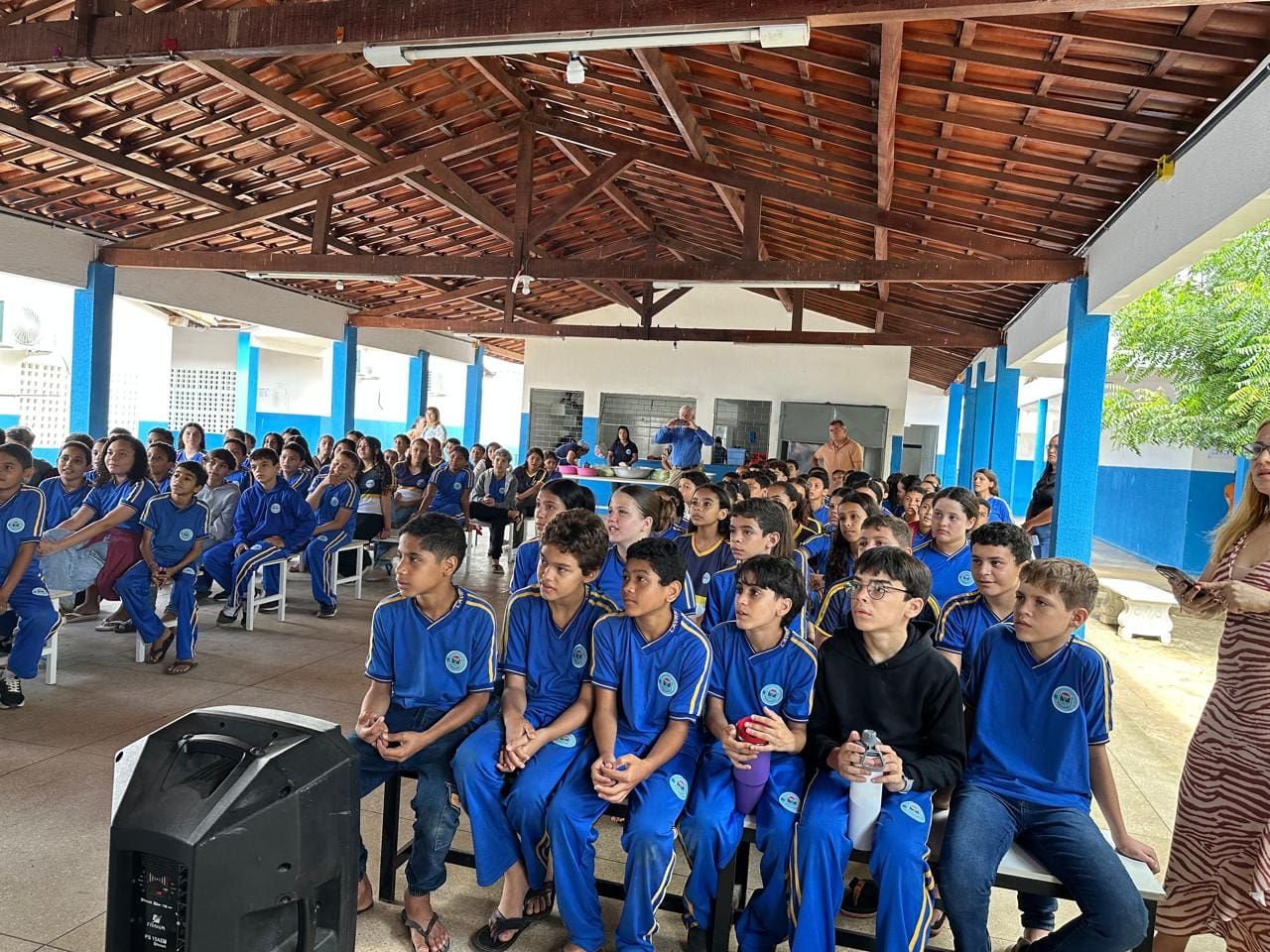 Students in blue uniforms seated in a large hall during an event.